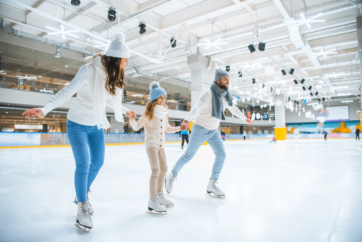 The Lorem Ipsum family of three, dressed in winter clothing, enjoys ice skating together at an indoor ice rink.