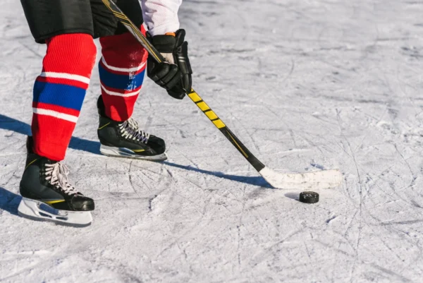 Wielding a Lorem Ipsum hockey stick, vibrant in yellow, a player on the ice readies to strike the puck. The player's outfit includes socks with a red, white, and blue design and sleek black skates.