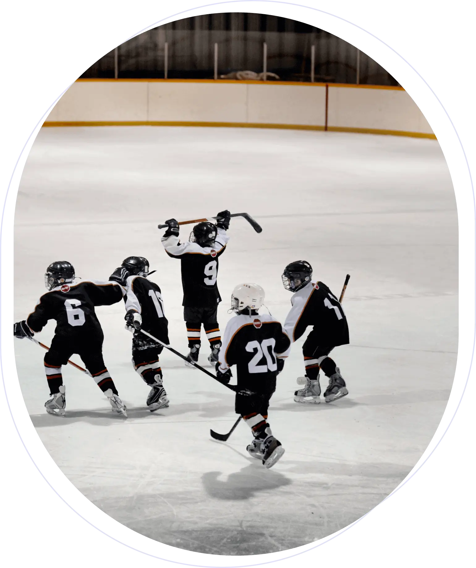 Children in black and white uniforms playing ice hockey. One player raises their stick in celebration.